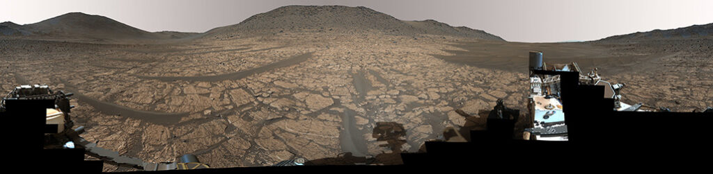 An image of a rock on Mars taken by the NASA rover Perseverance. Rocky white stripes flank a clay-colored area that is speckled with dark spots.